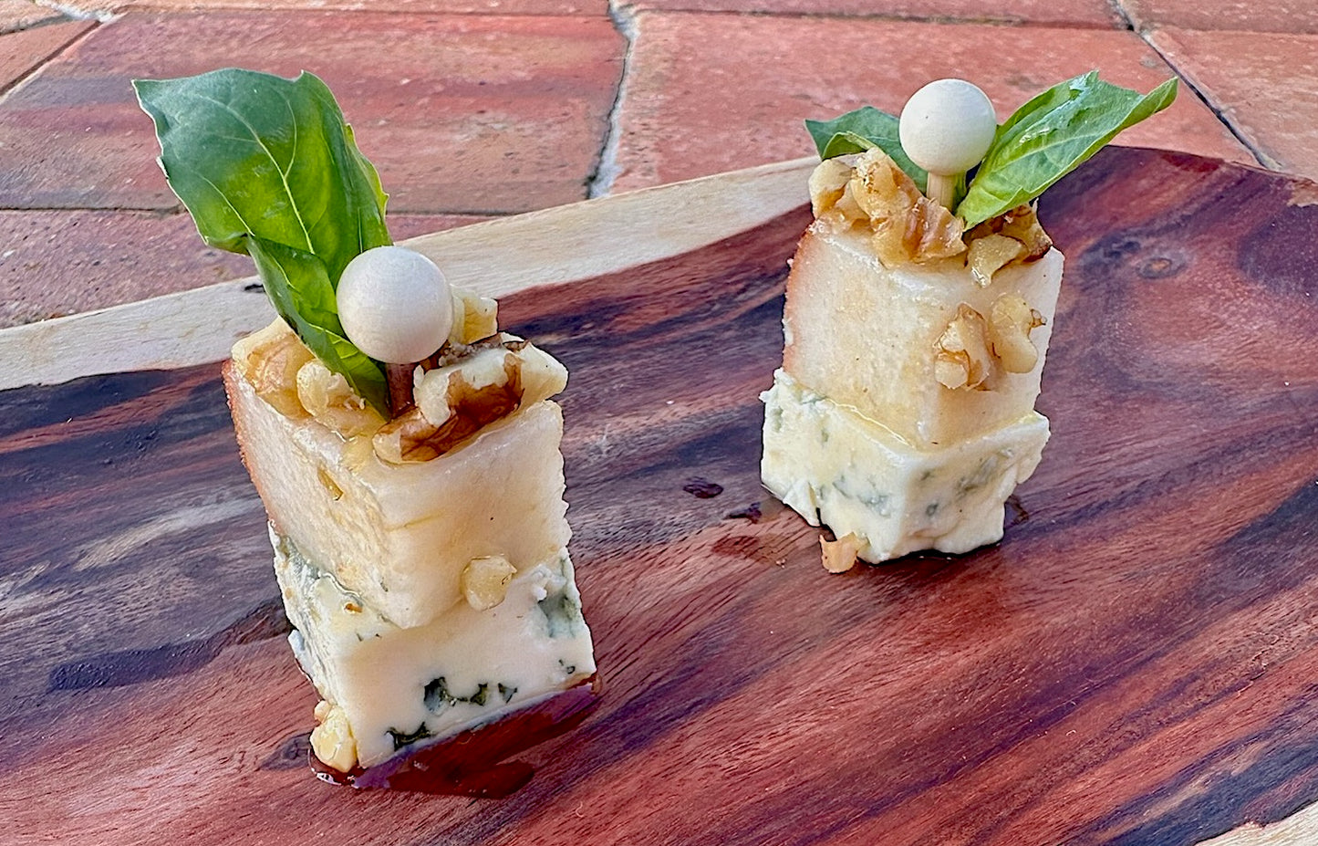 Premium Danish Blue Cheese canapés, topped with roasted walnuts, a green basil leaf, and a drizzle of pure honey.