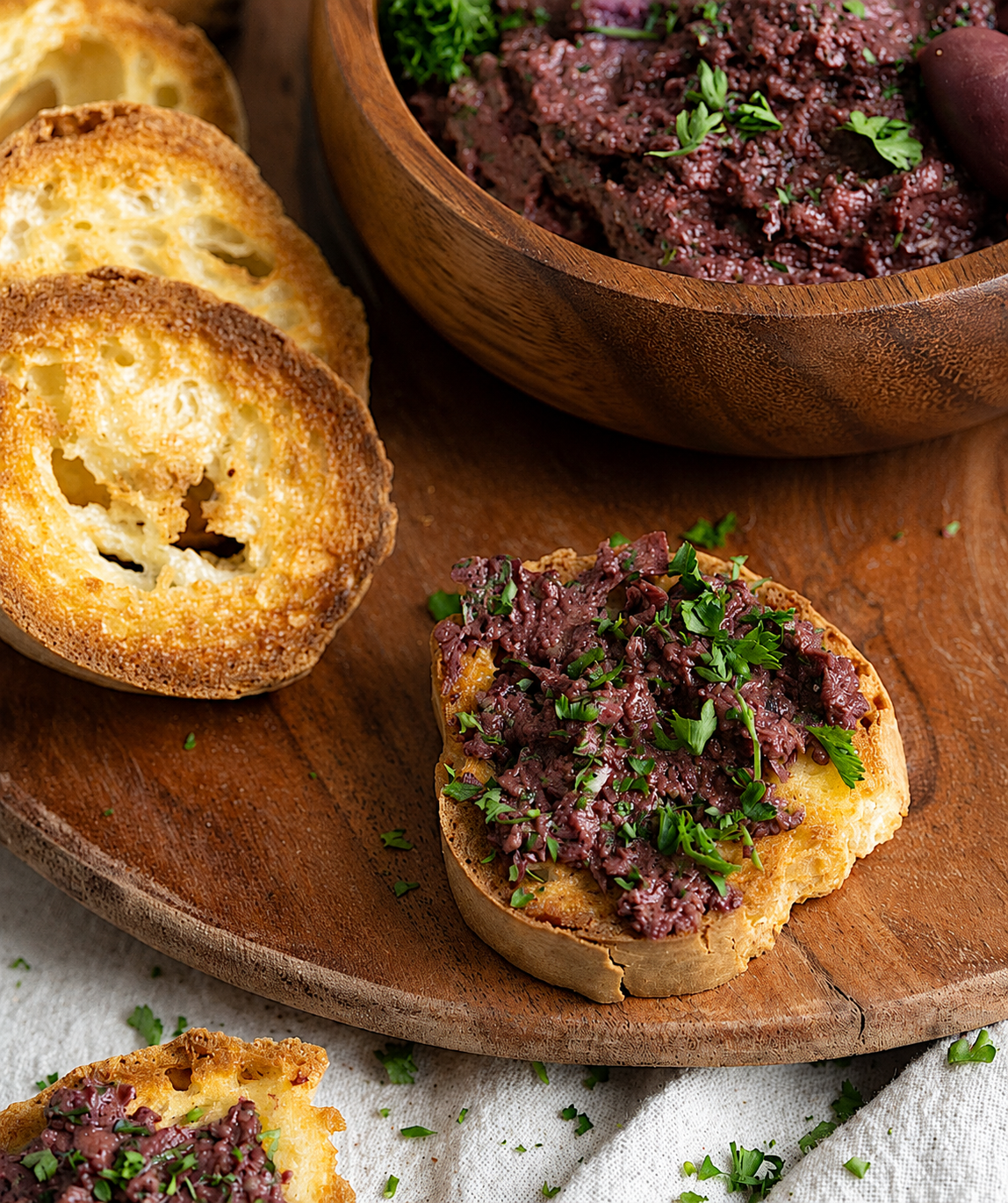 Slices of french bread crostinis topped with Kalamata Olive  spread and chopped herbs.