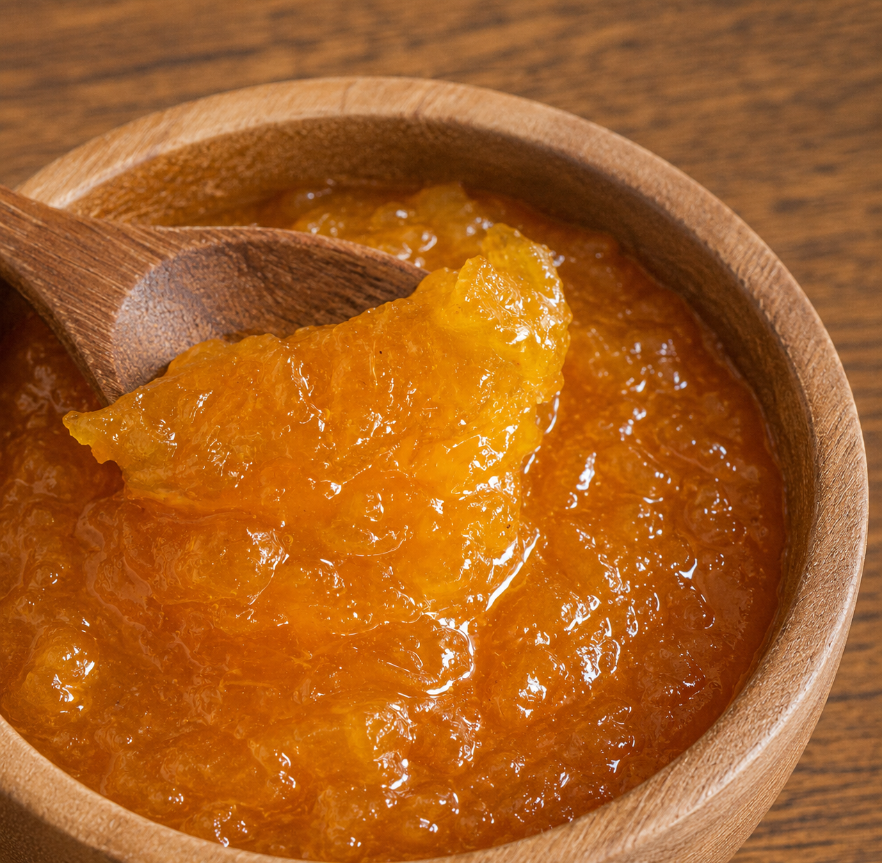 A close-up of a wooden bowl filled with glossy pineapple preserves, with a wooden spoon lifting a chunky piece of the preserve.